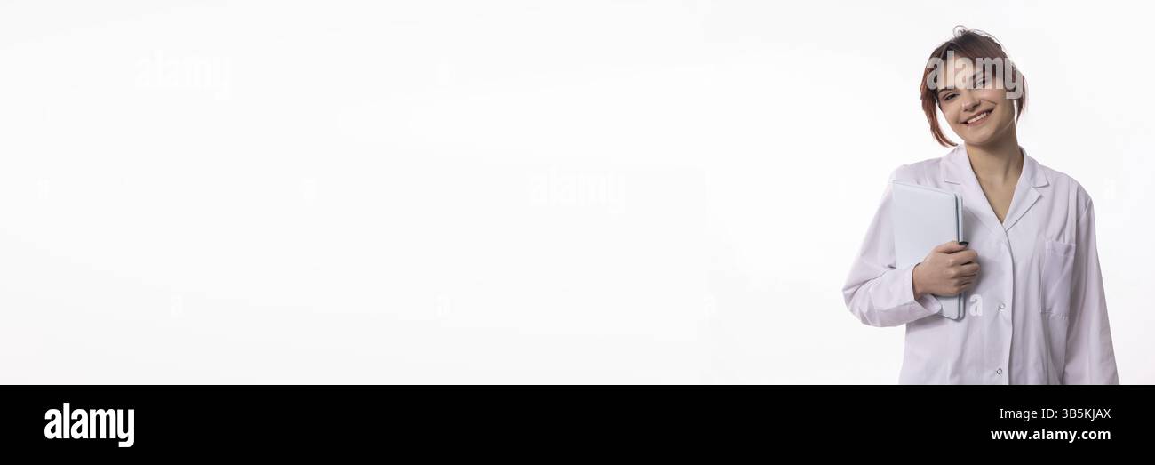 Ein junger Profi, der einen Laborkittel trägt, hält selbstbewusst ein Tablet und lächelt dabei fesselnd und fröhlich Stockfoto