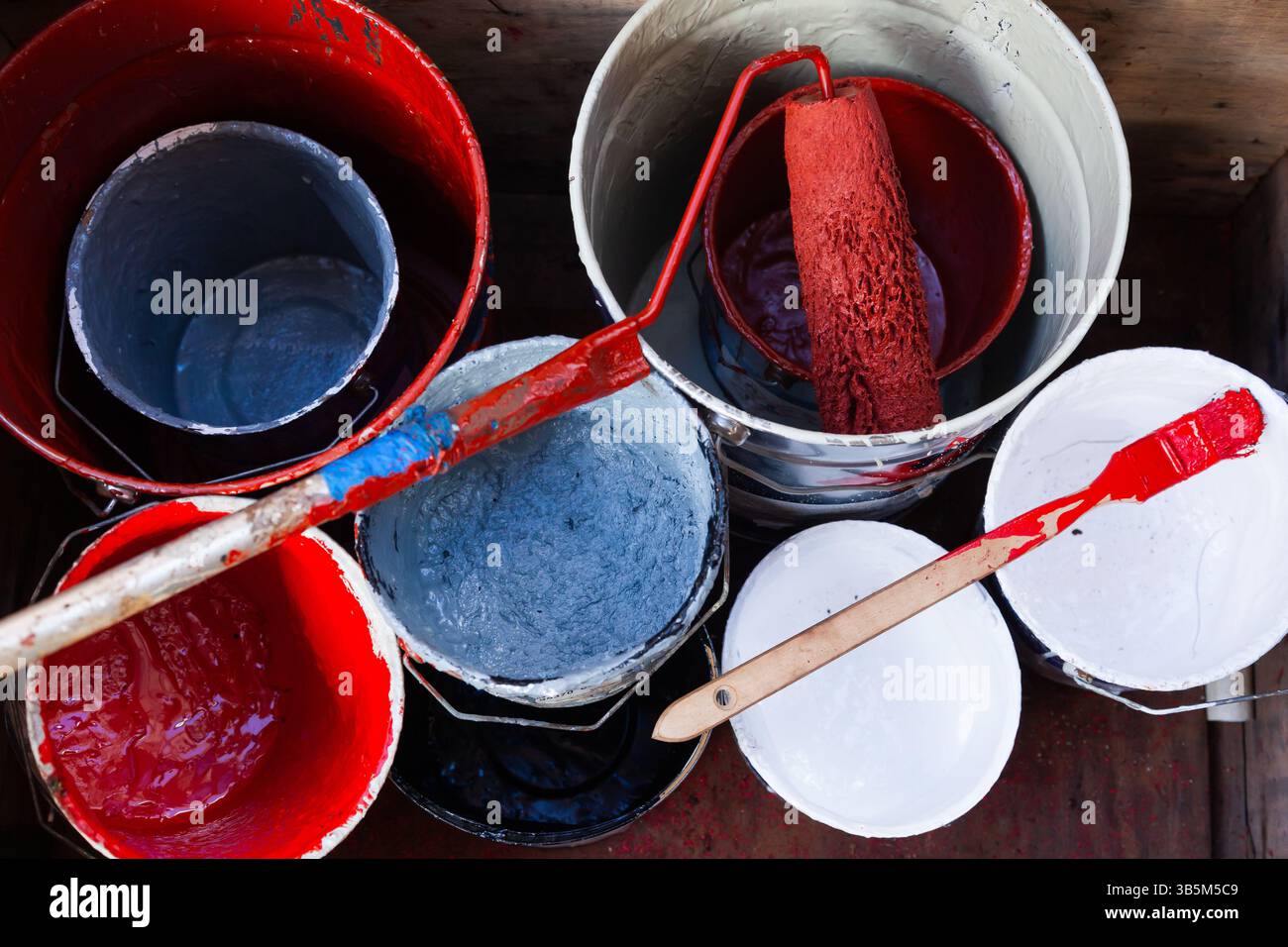 Leere Eimer mit Farbe in verschiedenen Farben und eine Rolle und ein Pinsel mit roter Farbe, Draufsicht. Stockfoto