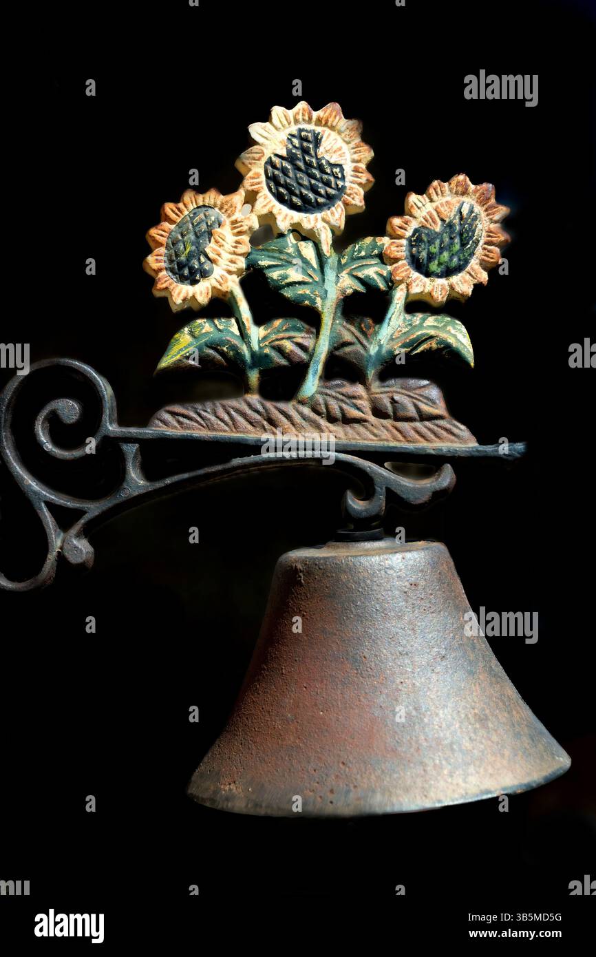 Eine wunderschön gefertigte Glocke hängt an einer Eisenhalterung mit fröhlichen Sonnenblumen in leuchtenden Farben. Das rustikale Dekor unterstreicht den Charme des Ausflugs Stockfoto