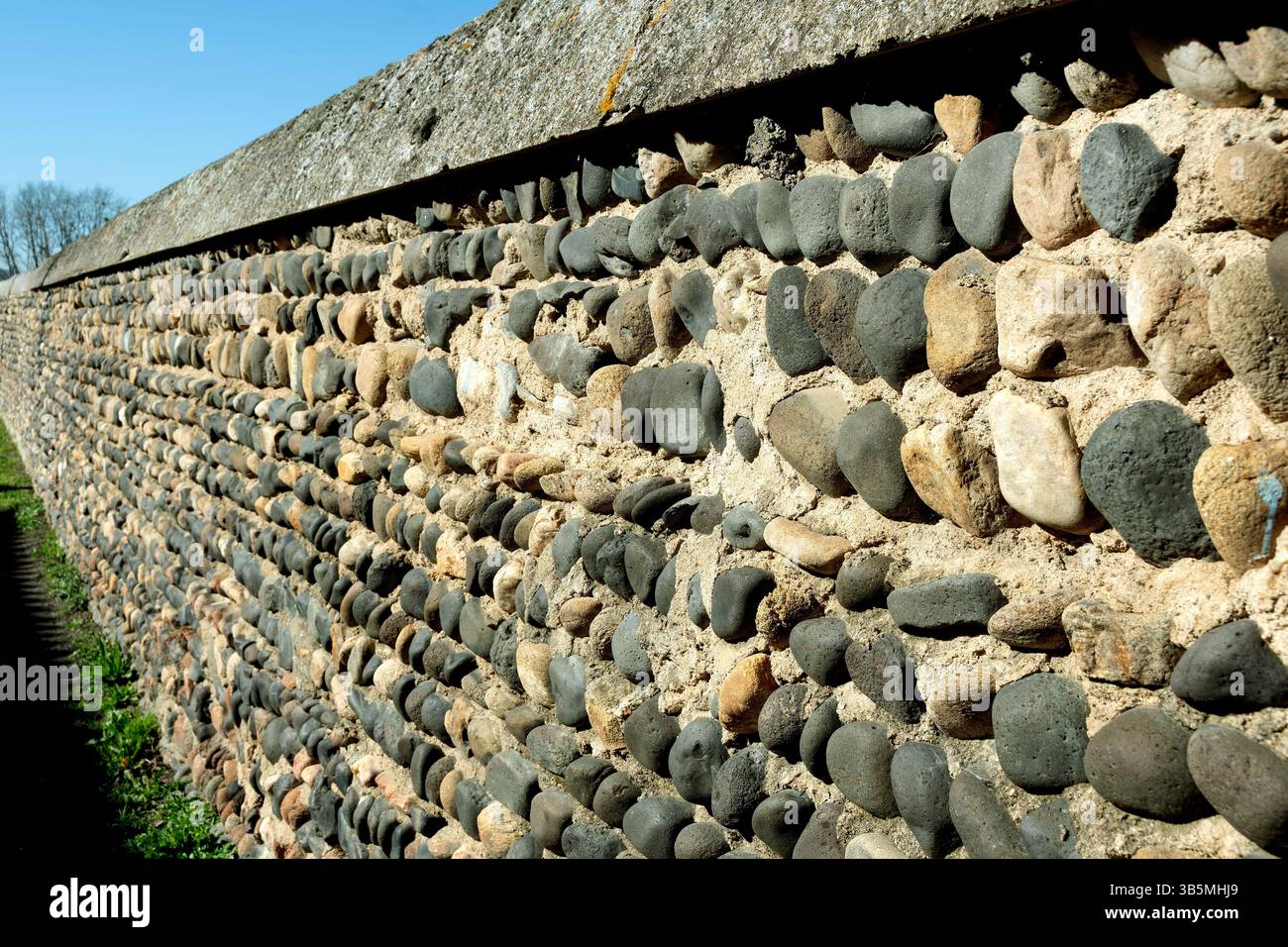 Die Nahaufnahme einer Steinmauer aus verschiedenen Kieselsteinen und Kopfsteinpflastern schafft eine interessante Textur vor dem klaren blauen Himmel. Frankreich Stockfoto