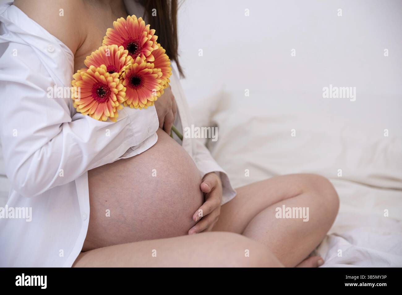 Eine schöne schwangere Frau wiegt ihren Bauch sanft mit leuchtenden Blumen, die neues Leben und Mutterschaft symbolisieren Stockfoto