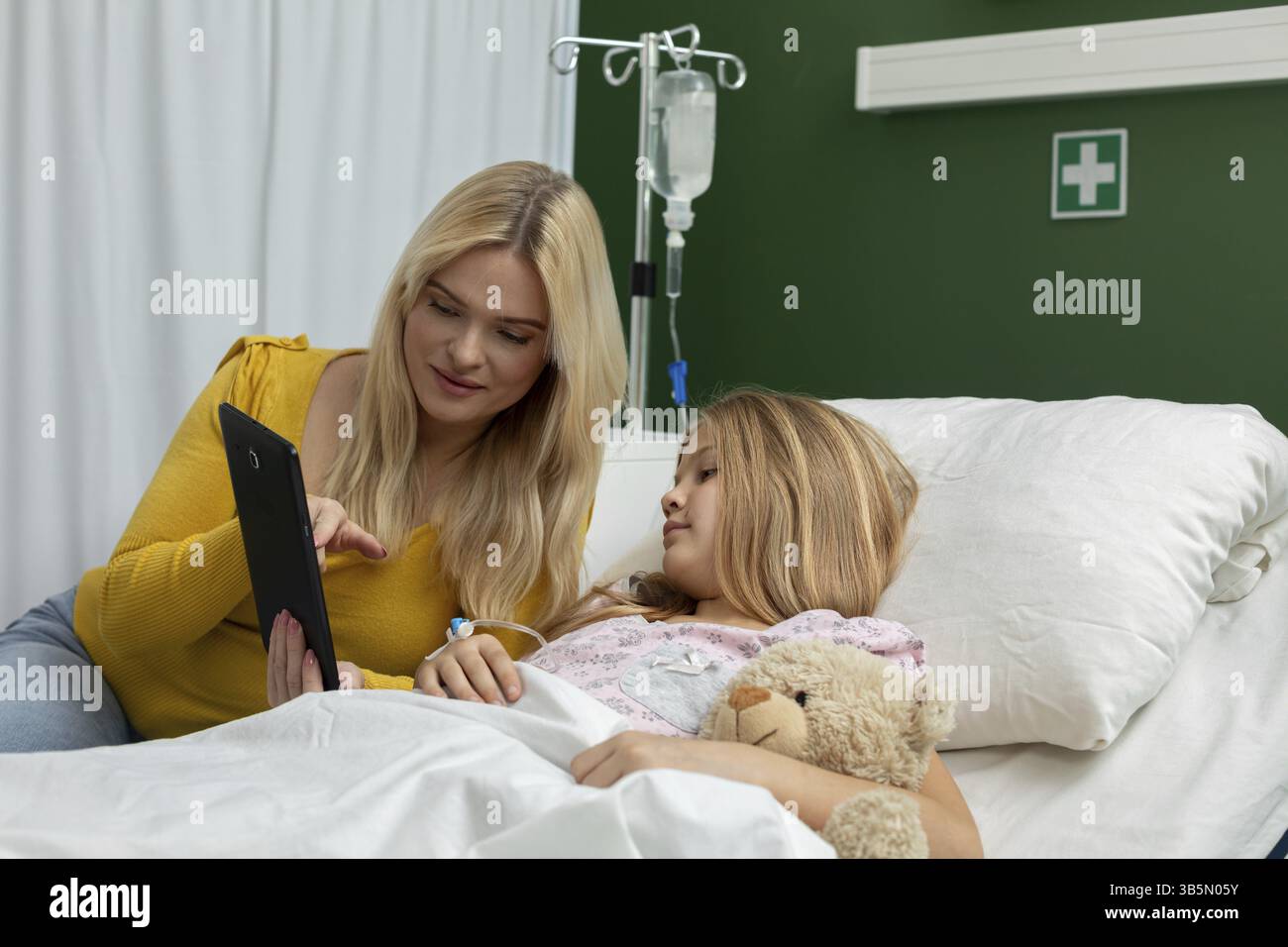Eine junge Frau tröstet einen Patienten in einem Krankenhausbett mit einem Tablet und hebt Pflege und Verbindung hervor Stockfoto