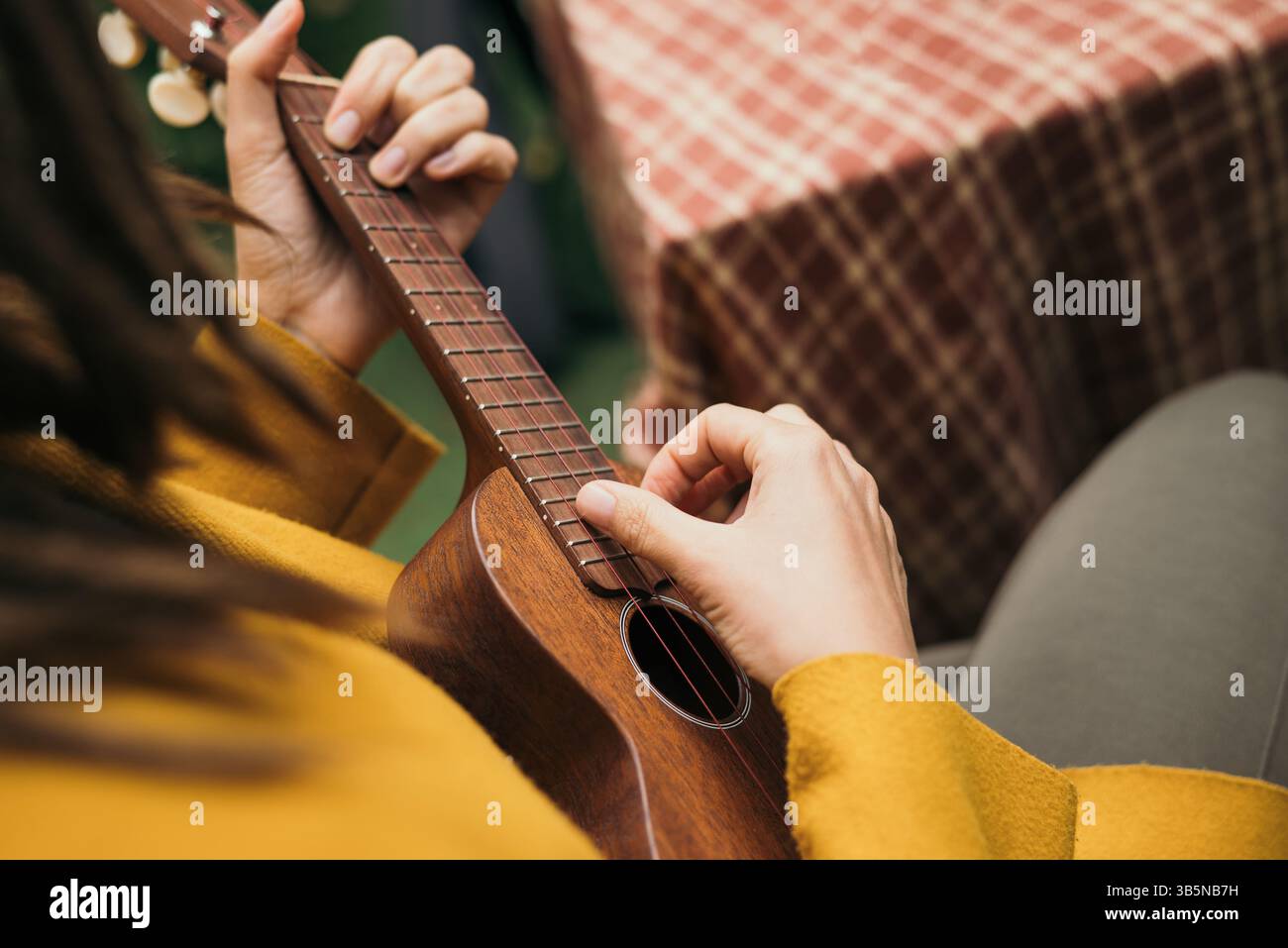 Mädchen mit Dreadlocks aus der Nähe spielt im Herbst auf der Terrasse ein Akustikinstrument Ukulele. Stockfoto