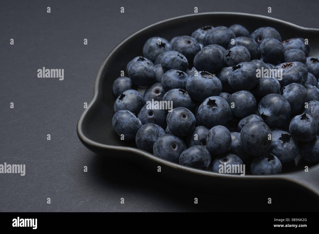 Heidelbeeren auf einer schwarzen Tonpfanne mit schwarzem Hintergrund, Nahansicht Stockfoto