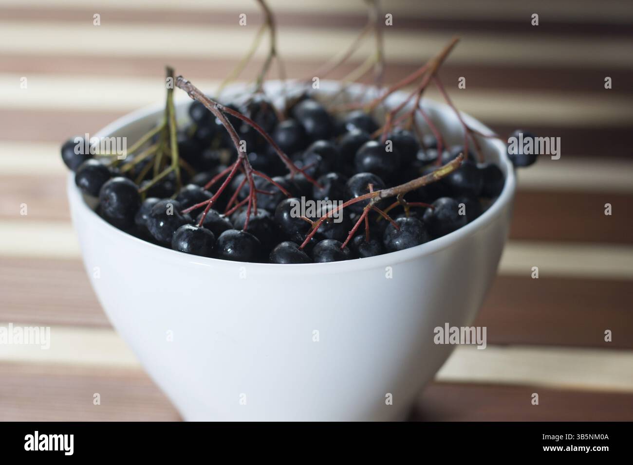 Nahaufnahme des nassen Aronia Beeren in Weiß einfache Schüssel auf hölzernen Tisch Stockfoto