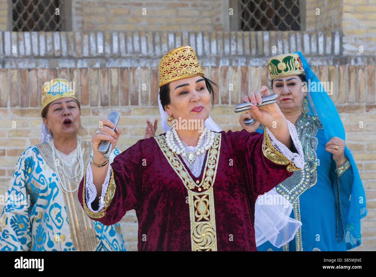 Usbekische Damen in traditioneller Kleidung spielen Qairaqs (flache ovale Steine) ähnlich wie Kastanetten vor mir-i-Arab Madrasa in Buchara, Usbekistan Stockfoto