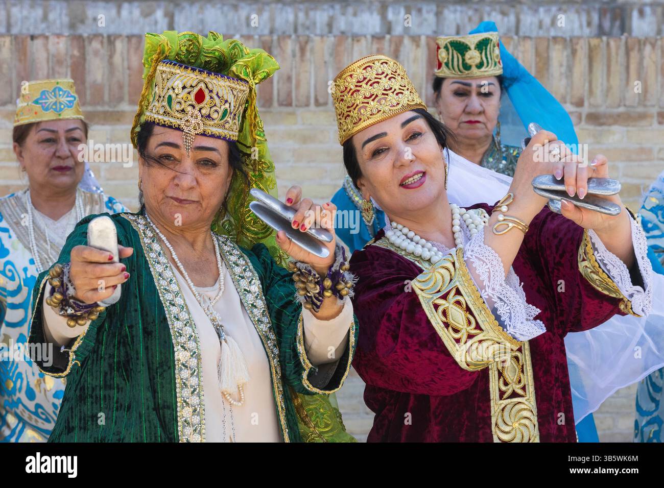 Usbekische Damen in traditioneller Kleidung spielen Qairaqs (flache ovale Steine) ähnlich wie Kastanetten vor mir-i-Arab Madrasa in Buchara, Usbekistan Stockfoto