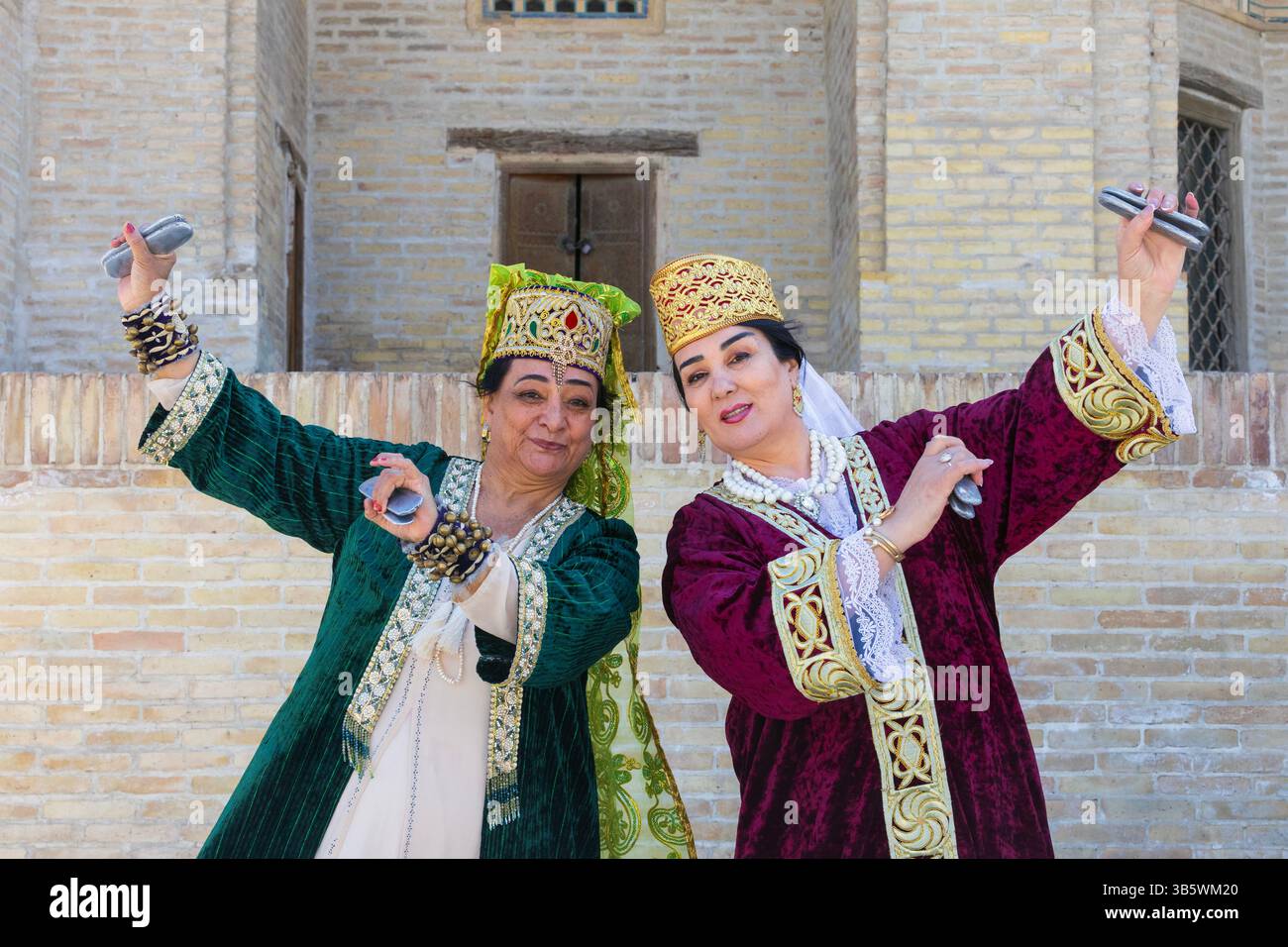 Usbekische Damen in traditioneller Kleidung spielen Qairaqs (flache ovale Steine) ähnlich wie Kastanetten vor mir-i-Arab Madrasa in Buchara, Usbekistan Stockfoto