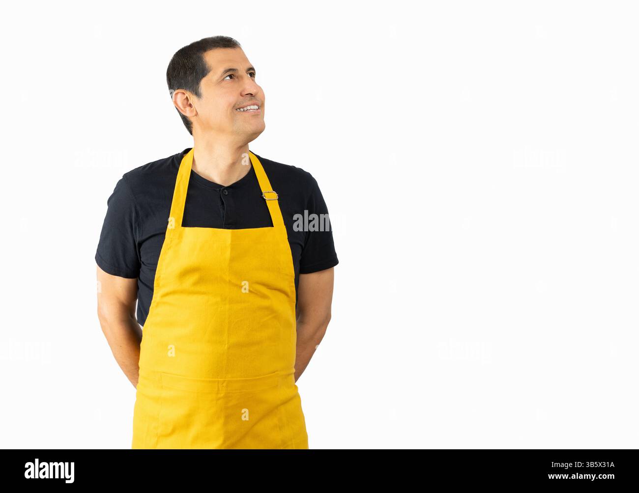 Lateinischer Mann mit gelber Schürze auf weißem Hintergrund schaut auf den Kopierraum, Lieferdienstmitarbeiter, Kellner in gelber Schürze Stockfoto
