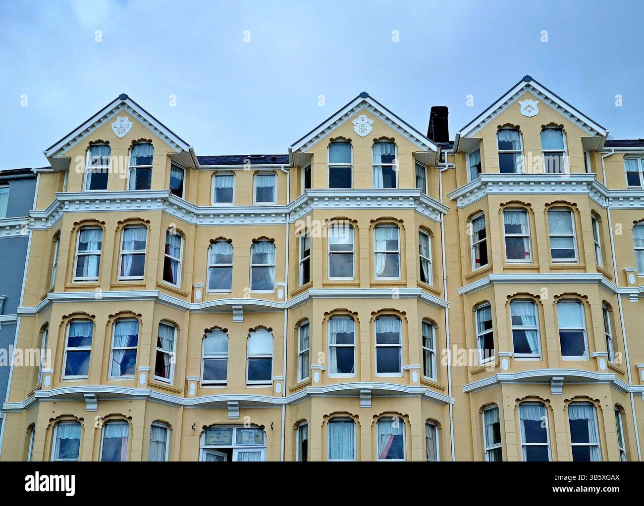 Beigefarbene Fassade eines Wohnhauses mit Erkerfenstern, weißen Stuckverzierungen und kunstvoll geschnitzten Fensteröffnungen an der Promenade in Douglas, Isle of man Stockfoto