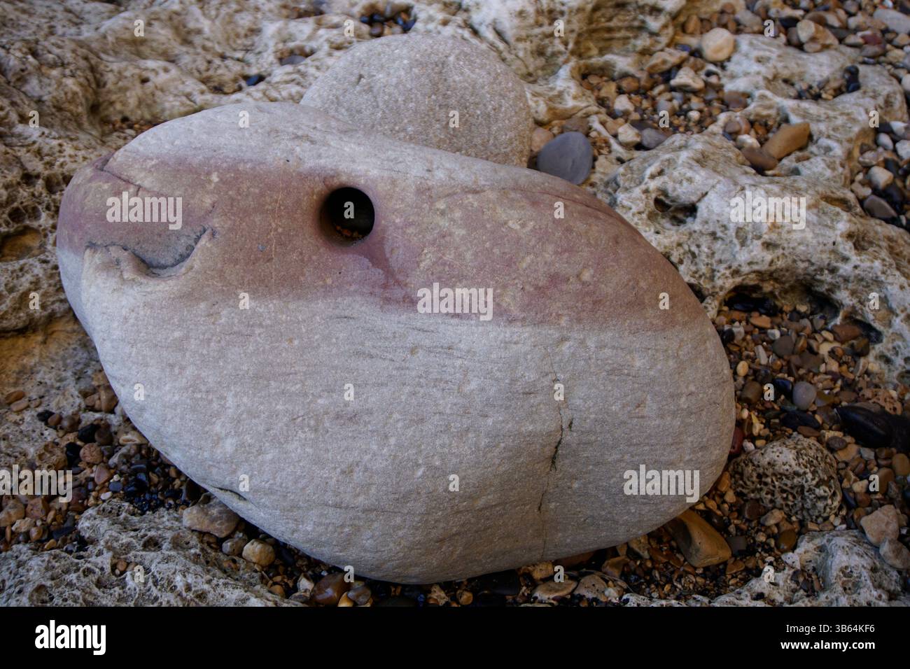 Erodiertes Sedimentgestein mit natürlichem Loch und farbigen Schichten an einem felsigen Strand. Seaham Beach, England Stockfoto