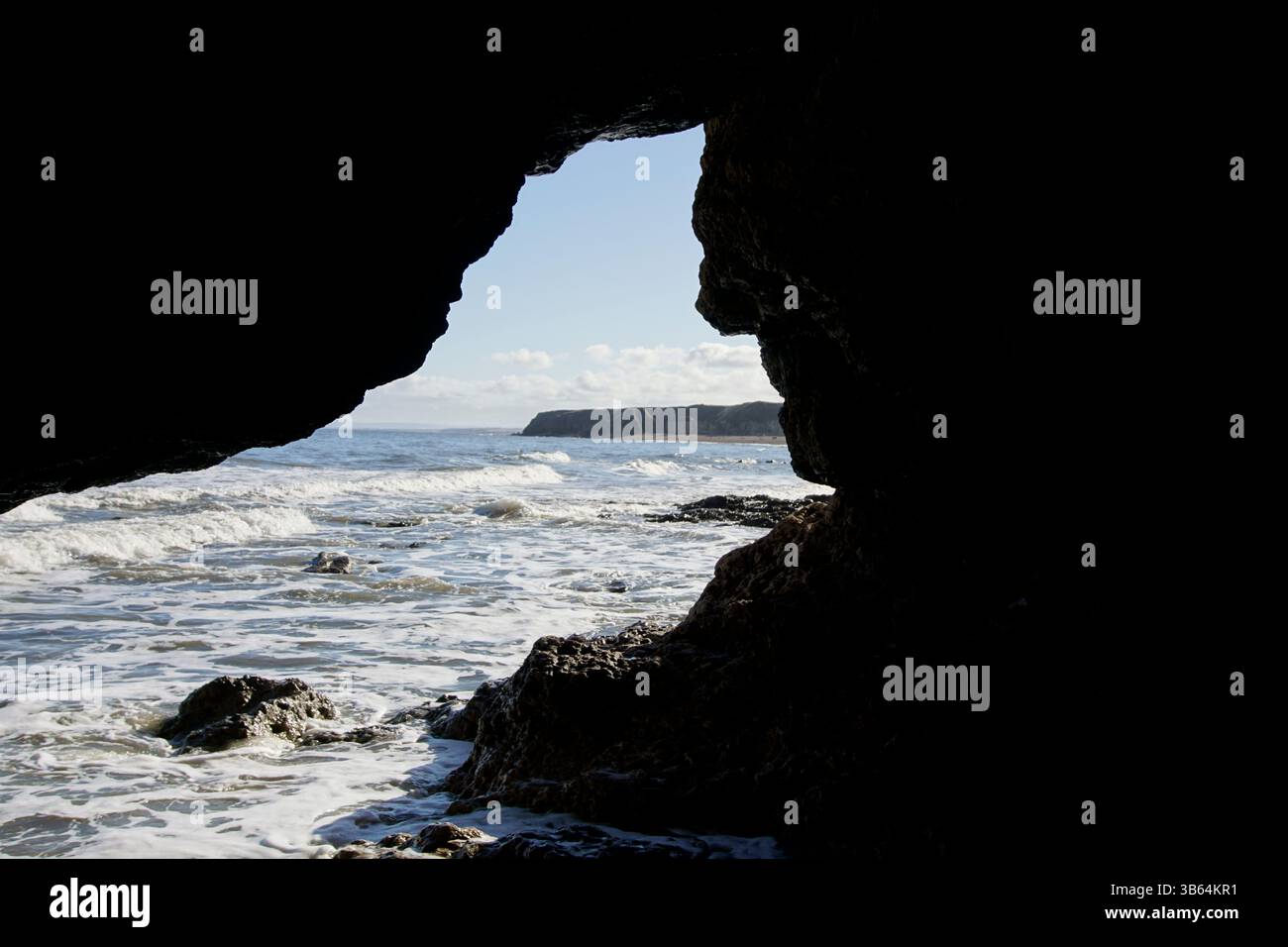 Ozeanwellen und ferne Klippen durch die Öffnung einer felsigen Meereshöhle. Seaham Beach, England Stockfoto