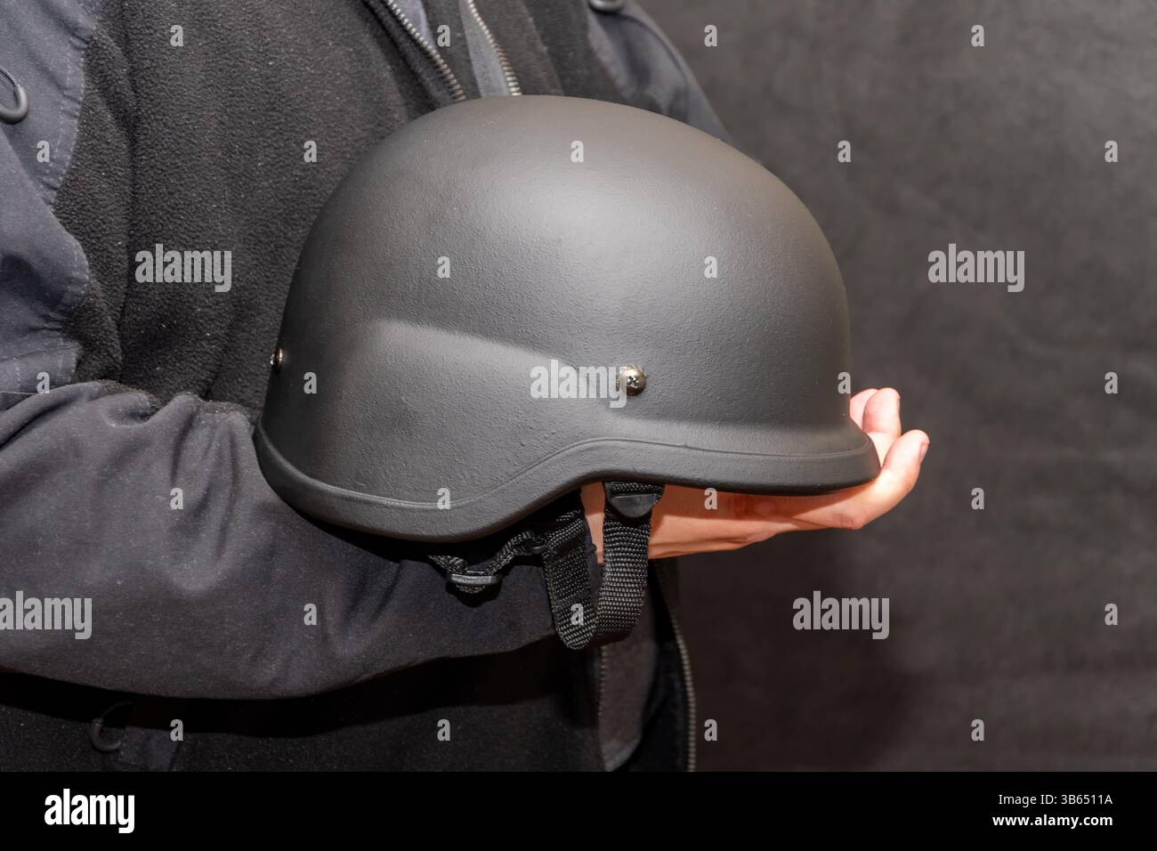 Ein Mann, der eine Körperpanzerung trägt, hält einen taktischen Militärhelm in der Hand Stockfoto