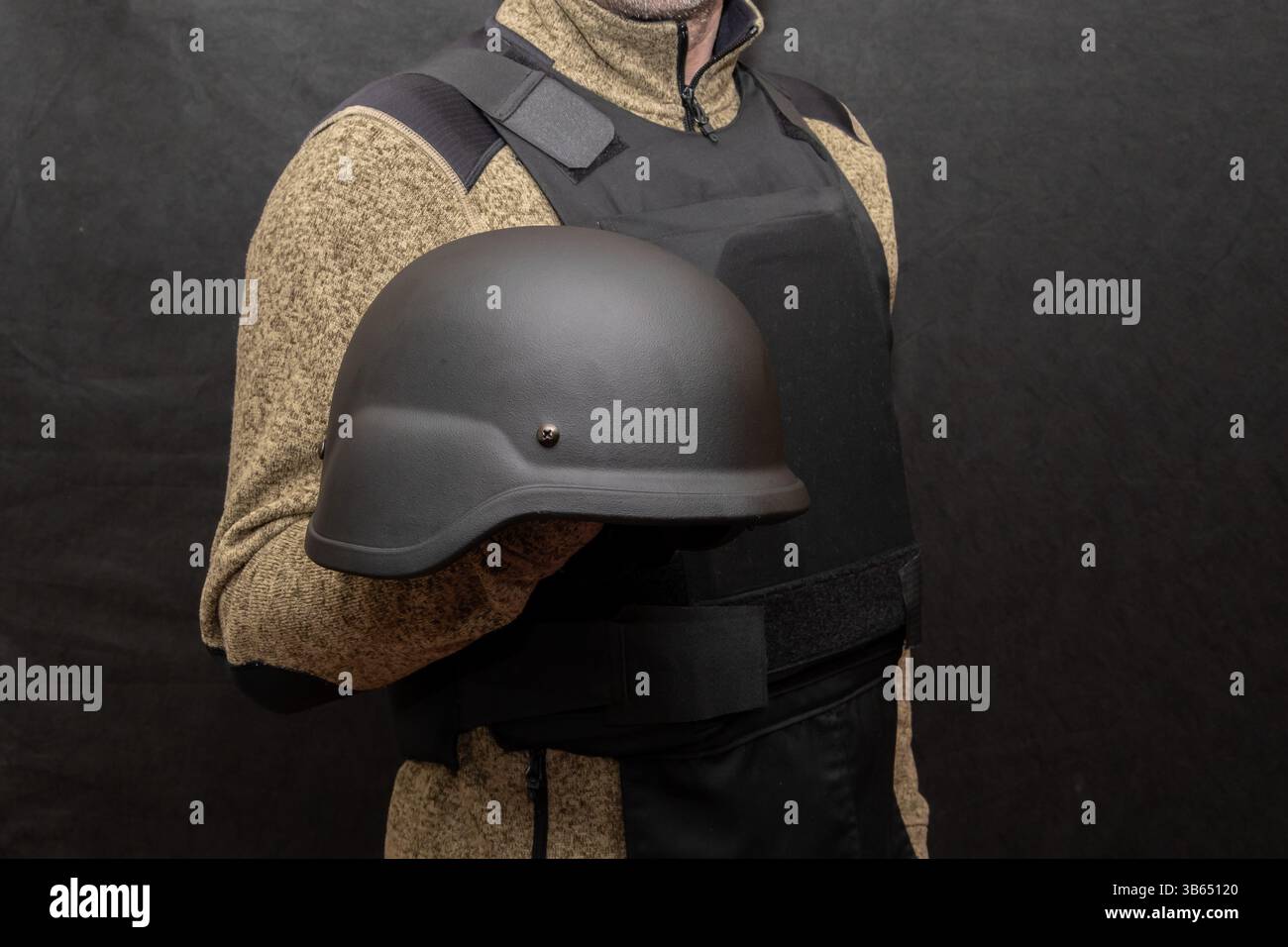 Porträt des Mannes in Körperpanzerung mit Helm in der Hand auf dunklem Hintergrund. Das Konzept des persönlichen Schutzes, der Ausbildung und der Verteidigung Stockfoto