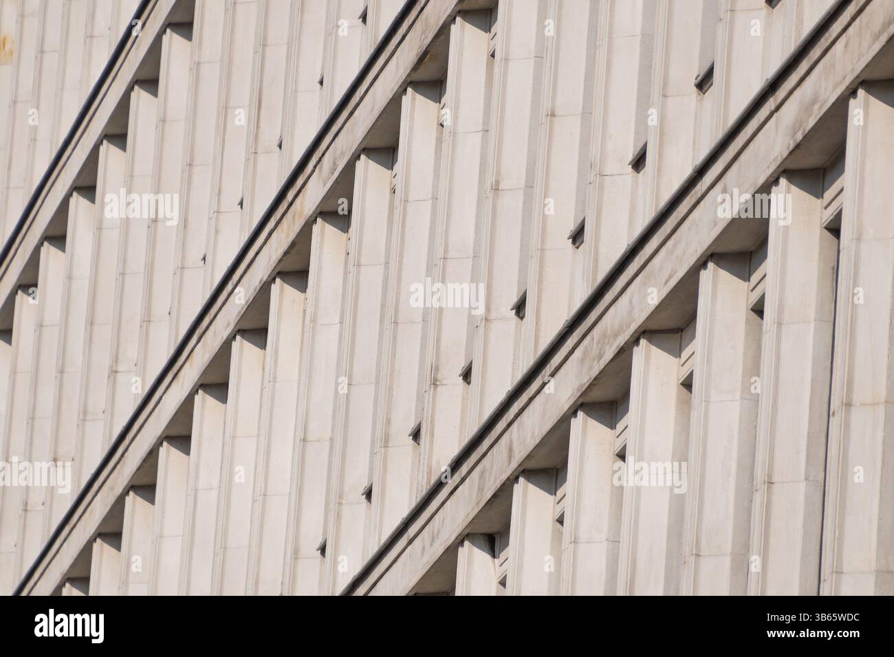 Eine modernistische Fassade mit sich wiederholenden vertikalen Betonelementen, die rhythmische Muster und dynamische diagonale Schatten erzeugen. Architekturdetails. Stockfoto