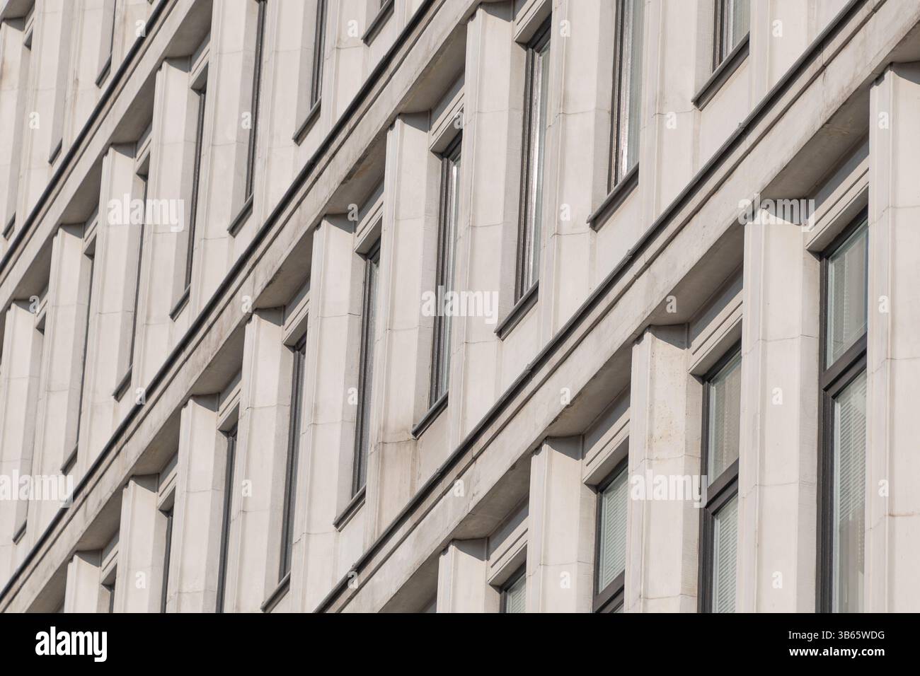 Eine modernistische Fassade mit sich wiederholenden vertikalen Betonelementen, die rhythmische Muster und dynamische diagonale Schatten erzeugen. Architekturdetails. Stockfoto