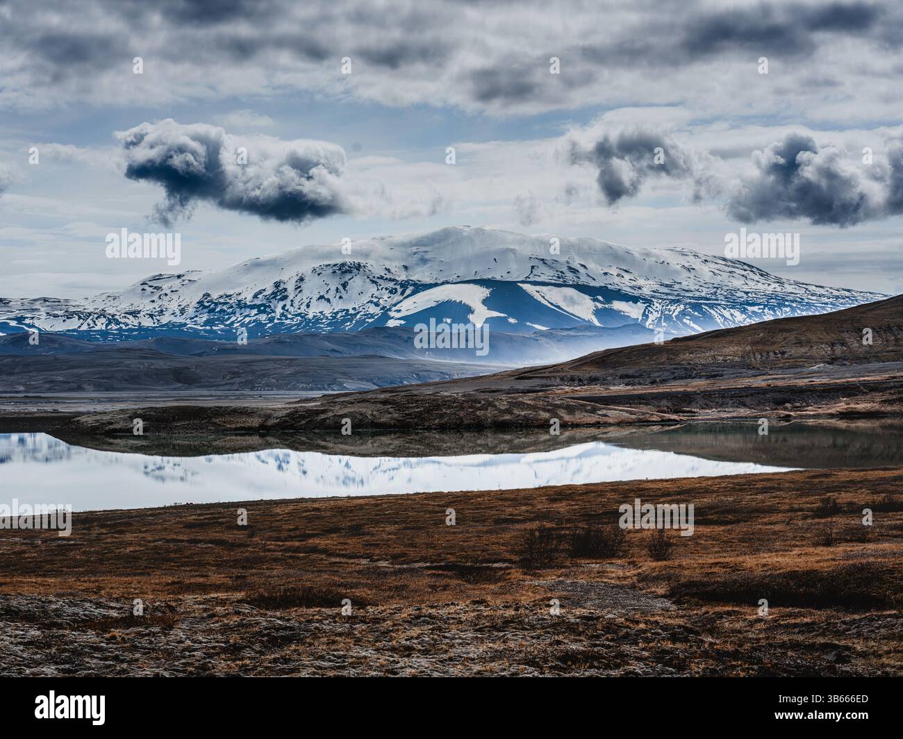 Schneebedeckter Berg spiegelt sich in einem stillen See unter einem stimmungsvollen Himmel im Osten Islands Stockfoto