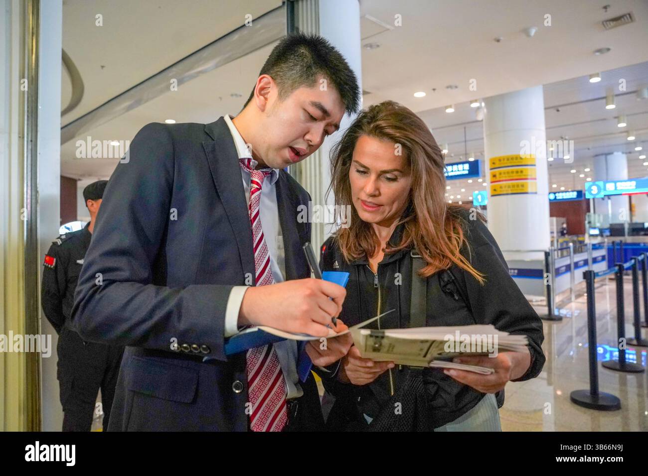 (250503) -- PEKING, 3. Mai 2025 (Xinhua) -- Ein Mitarbeiter der Tianjin-Niederlassung der Bank of China (BOC) stellt der russischen Touristin Anna am 1. Mai 2025 im Tianjin International Cruise Home Port in Tianjin, Nordchina, einen Leitfaden für Zahlungsdienste zur Verfügung. China hat am 27. April ein neues Maßnahmenpaket zur weiteren Optimierung der Politik zur Erstattung der Abreisesteuer und zur Steigerung der Ausgaben für eingehende Reisen eingeführt. Zu den Maßnahmen, die vom Handelsministerium und fünf anderen Regierungsstellen angekündigt wurden, gehören eine Senkung der Mindestbeschaffungsschwelle für Erstattungen, eine Anhebung der Obergrenze für die Barrückerstattung und eine Ausweitung des Netzes Stockfoto