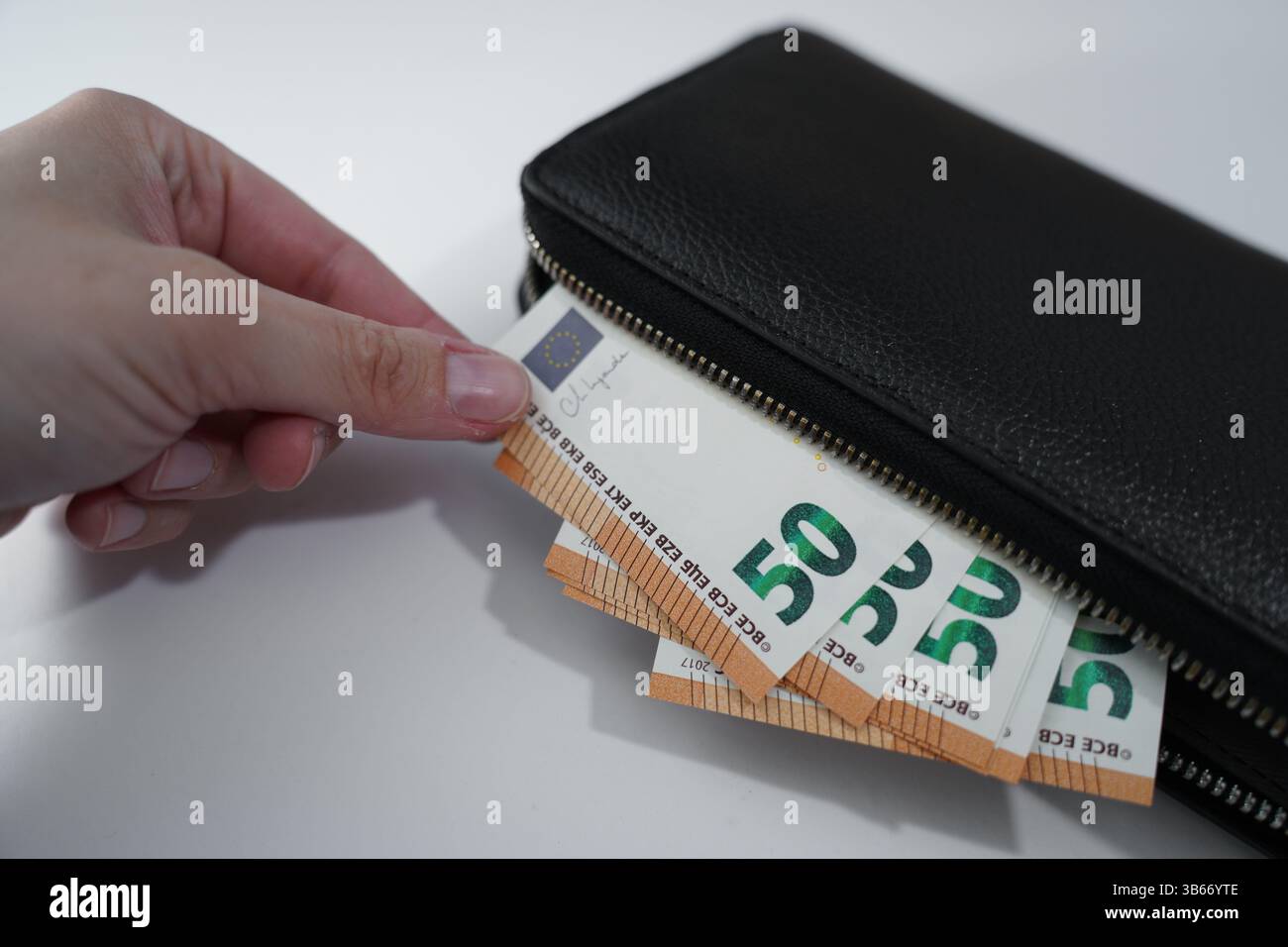 Eine Hand, die 50-Euro-Banknoten aus einer schwarzen Geldbörse auf weißem Hintergrund zieht, Finanzen und Ausgaben. Stockfoto
