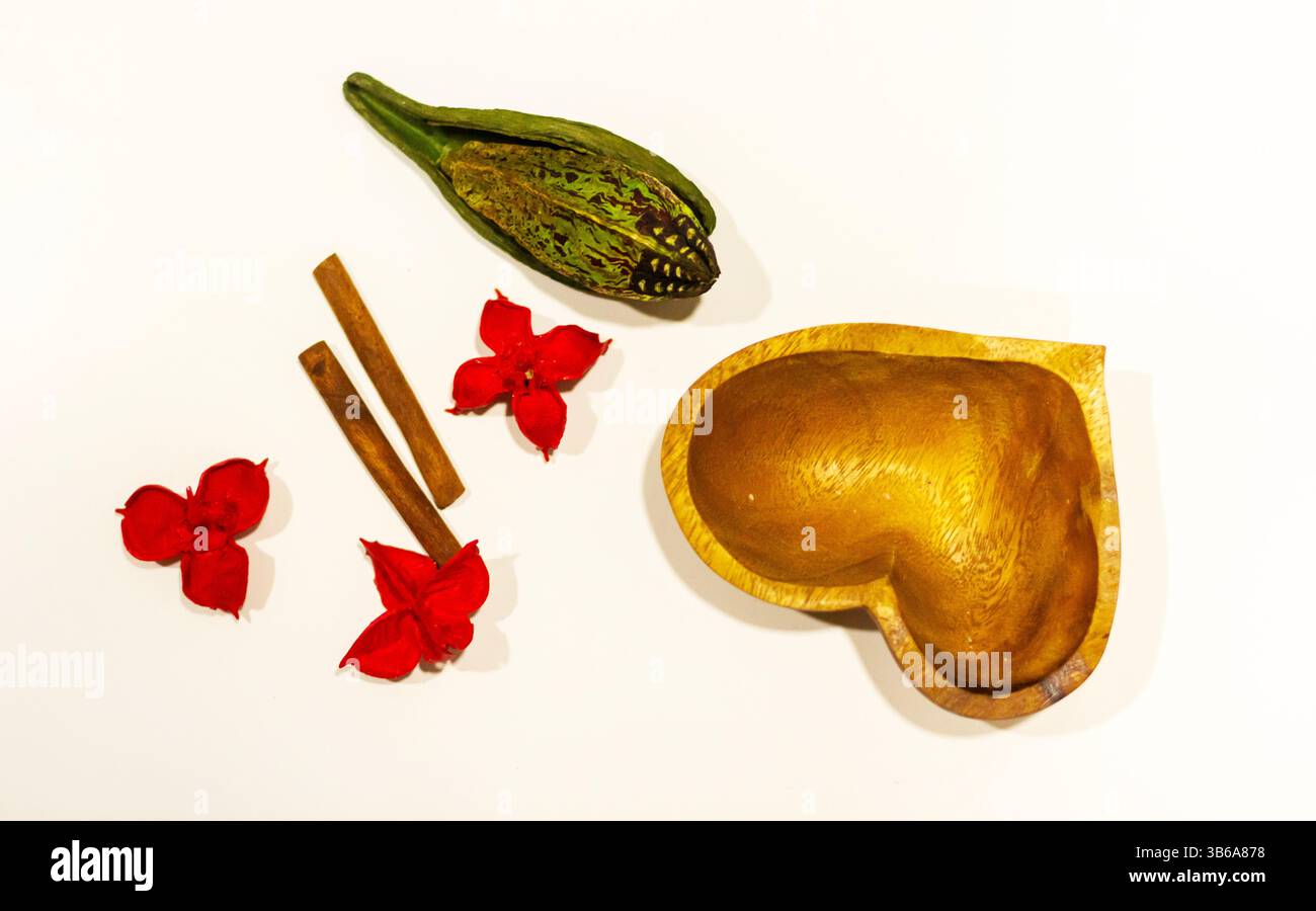 Eine schöne herzförmige Schüssel, die wunderschön von leuchtenden roten Blumen und aromatischen Zimtstäbchen umgeben ist und eine reizvolle Szene schafft Stockfoto