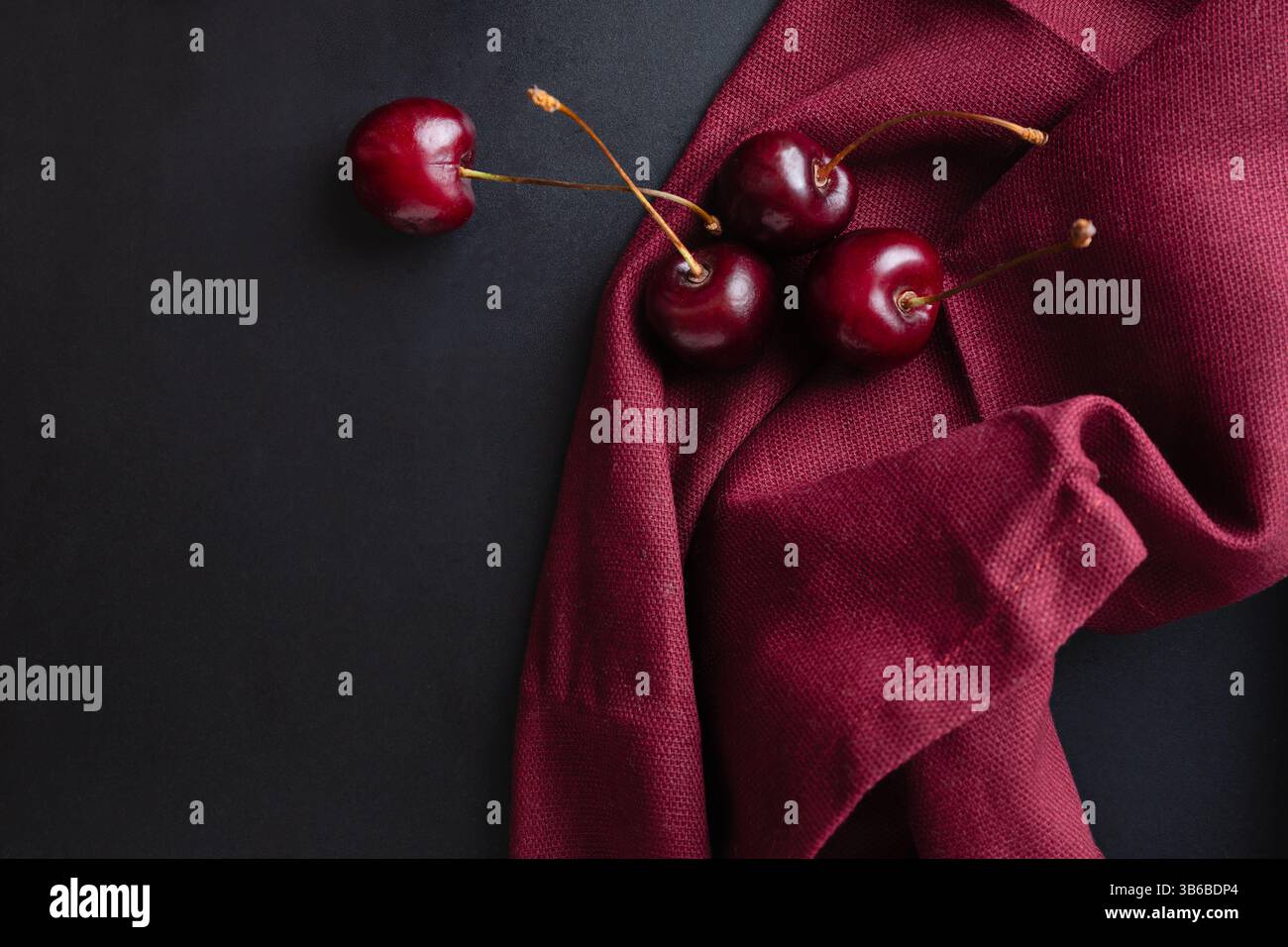 Reife Kirschen auf dunklem Hintergrund und burgunderblauem Stoff, eleganter Hintergrund mit Sommerbeeren Stockfoto