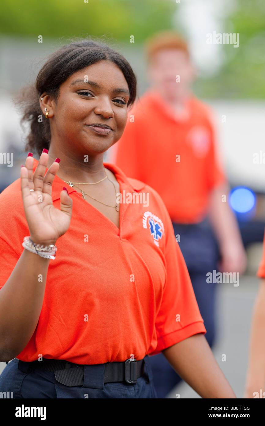 27. Mai 2024, Merrick, New York, Vereinigte Staaten: Junge Frau mit orangefarbenem Bellmore-Merrick Emergency Services EMS-Shirt winkt den Zuschauern während der Merrick Memorial Day Parade auf Long Island. (Bild: © Ann Parry/ZUMA Press Wire) Stockfoto