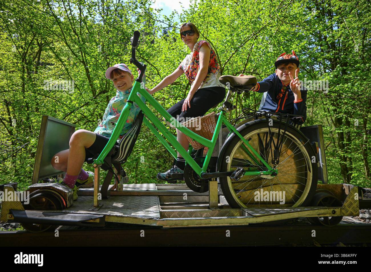 Die Familie genießt einen sonnigen Tag und radelt mit dem Fahrrad durch einen üppigen grünen Wald auf einer alten Eisenbahnstrecke. Stockfoto