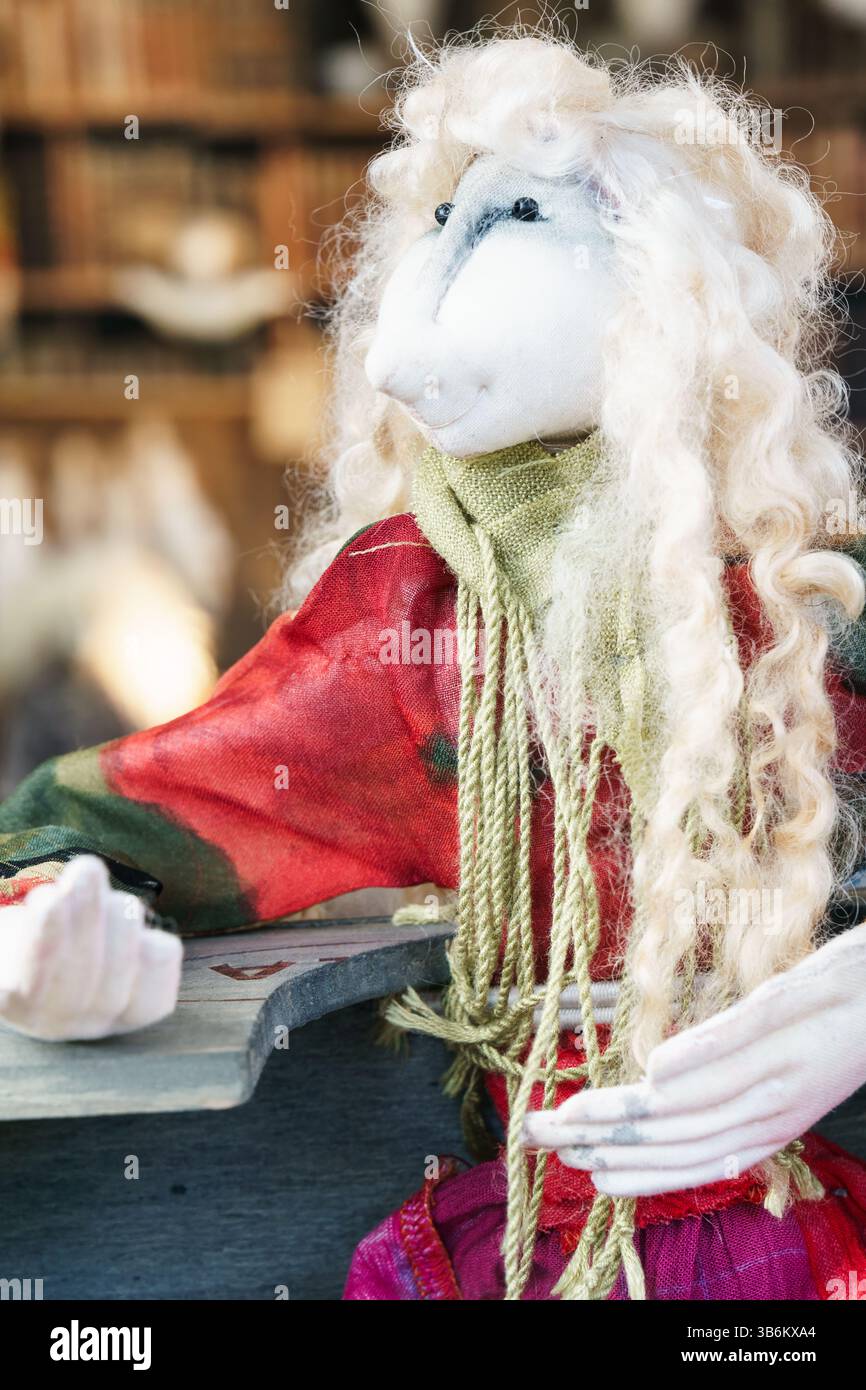 Nahaufnahme einer handgefertigten Puppe mit langen blonden lockigen Haaren, farbenfrohen Kleidern und grünem Schal, die auf eine Holzoberfläche gelehnt ist Stockfoto