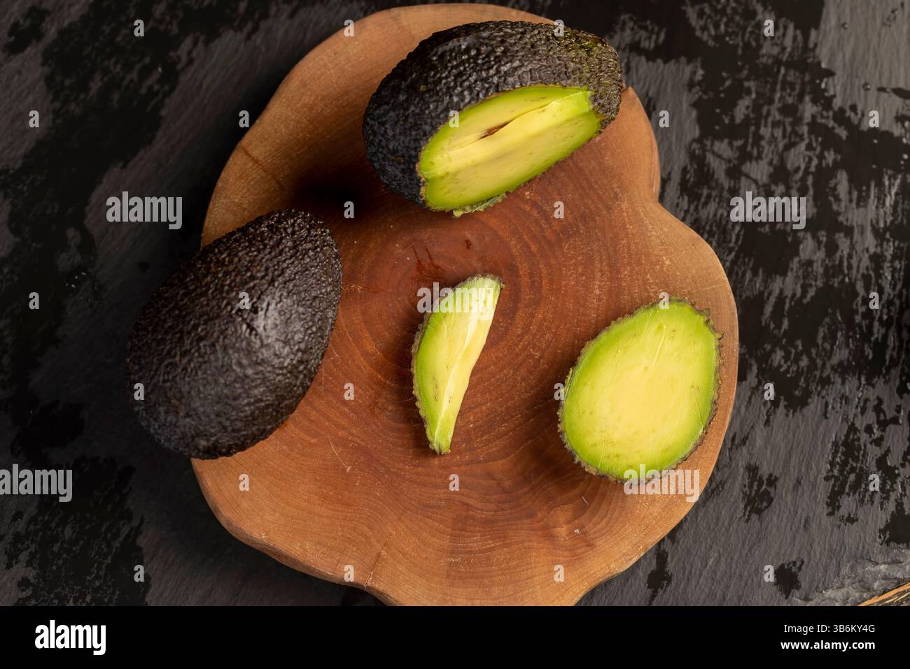 Avocado mit grünem Fleisch auf einem hölzernen Kirschbrett schneiden, kleine Avocado mit weichem überreifem Fleisch auf einem Brett in Scheiben schneiden, Nahaufnahme Stockfoto