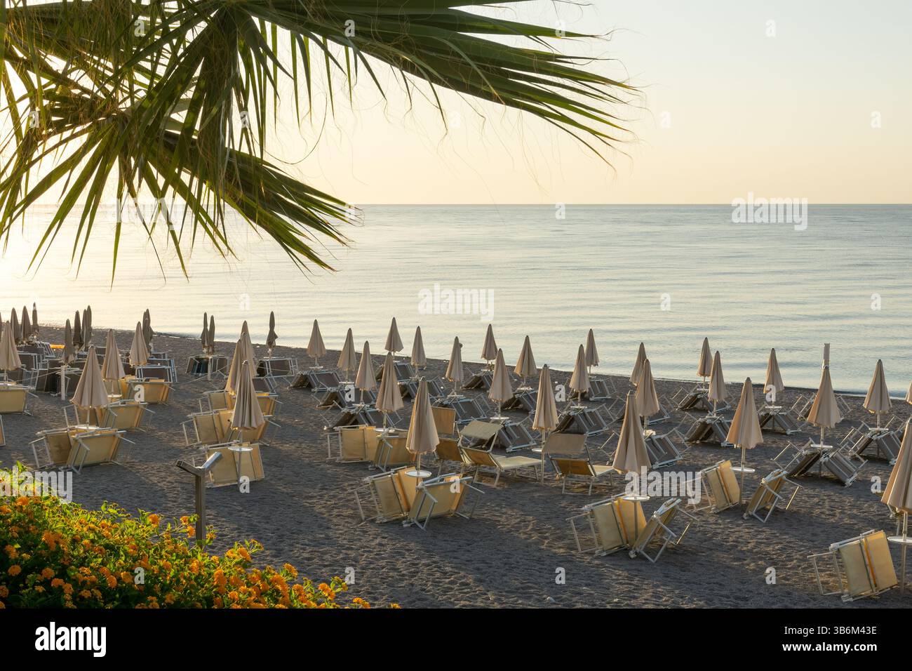 Ruhige Strandszene mit geschlossenen Sonnenschirmen und Liegestühlen bei Sonnenaufgang, die ein Gefühl der Ruhe und Erwartung wecken Stockfoto