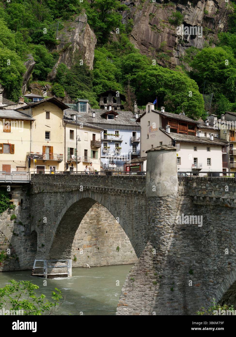 Brücke über den Fluss Dora Baltea und das Dorf Bard mit steilen Klippen dahinter im Aostatal, Italien, 3. Mai 2025 Stockfoto