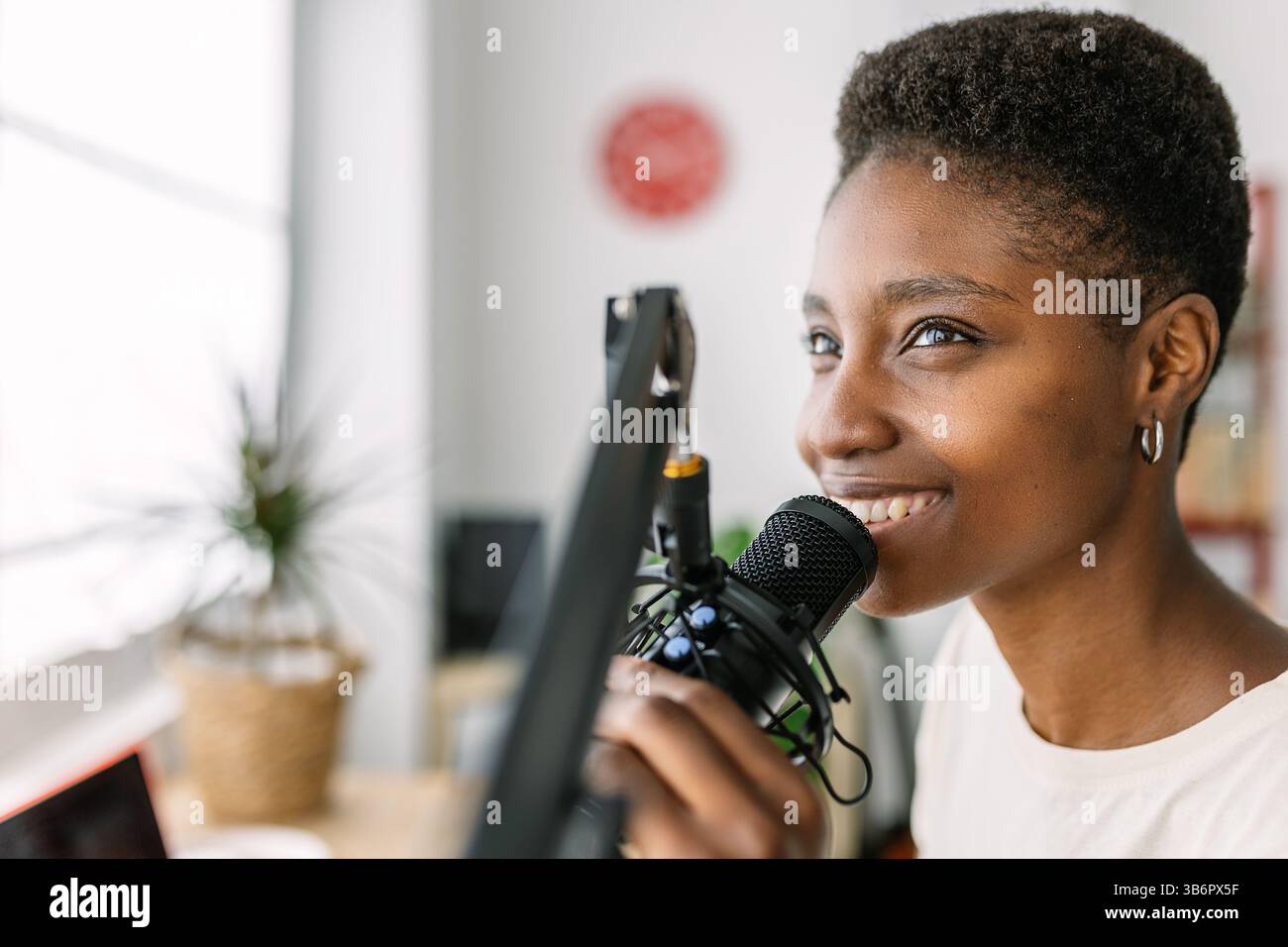 Lächelnde junge Podcasterin, die Radio-Podcast aus dem modernen Heimstudio aufnimmt Stockfoto
