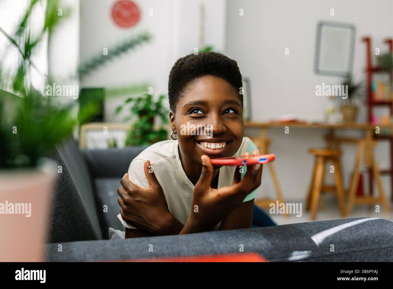 Glückliche schwarze Frau, die zu Hause den Sprachassistenten auf dem Smartphone benutzt Stockfoto