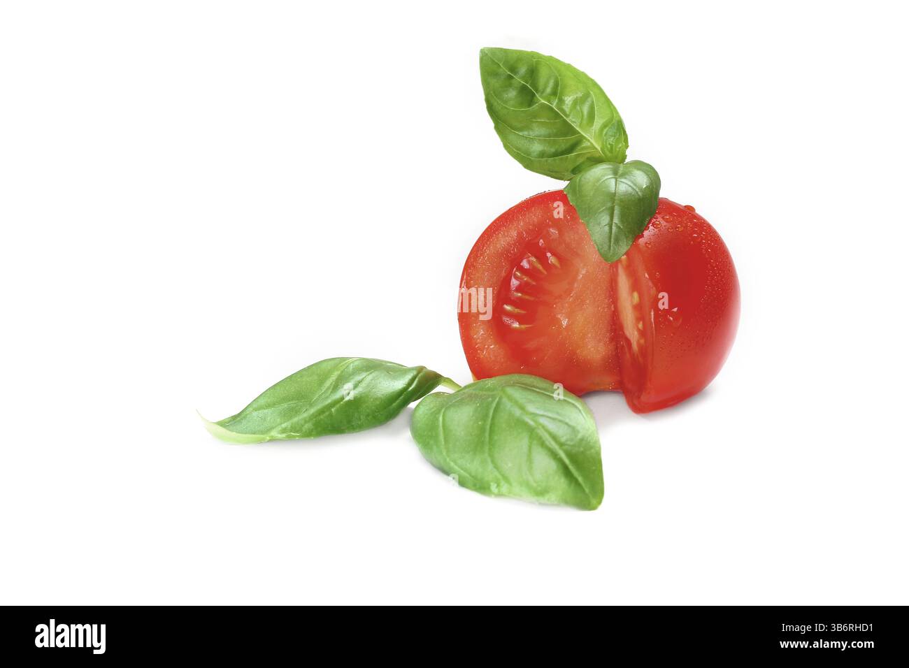 Eine leuchtend rote Tomate wird halbiert und offenbart ihr saftiges Inneres, während frische Basilikumblätter ein wenig Grün hinzufügen, was ein Gefühl von Frische weckt Stockfoto