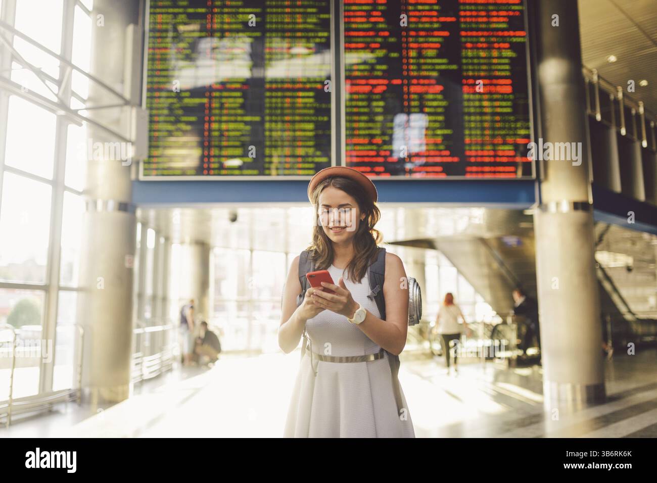 Thema Reisen und tranosport. Schönen jungen kaukasischen Frau in Kleid und Rucksack im Bahnhof oder Terminal auf einen Zeitplan fei Stockfoto