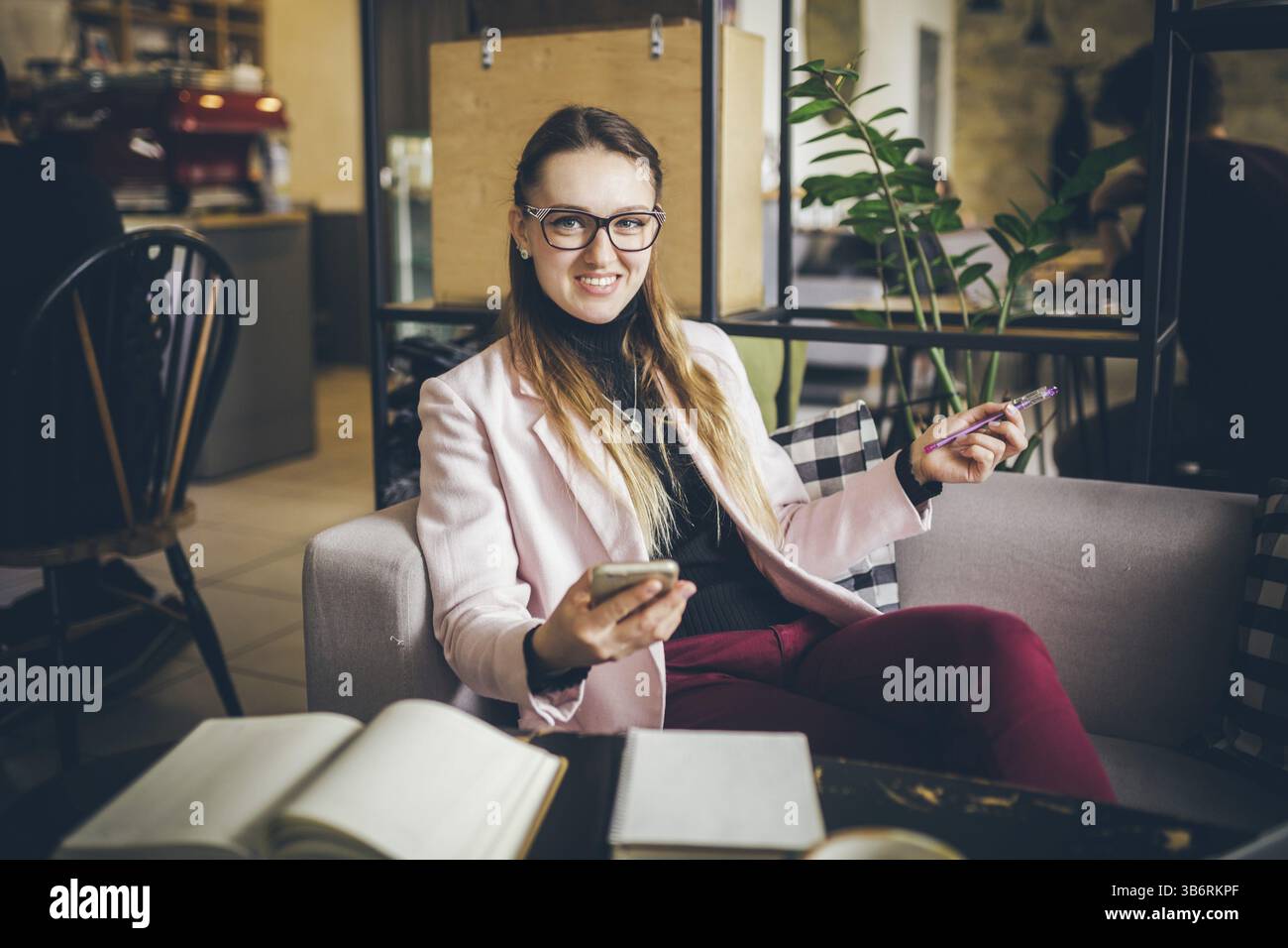 Thema moderner Beruf Bloggerin. Kaukasische Frau mit Brille und Jacke sitzt im Café hinter Holztisch mit Notizbuch, Laptop A Stockfoto