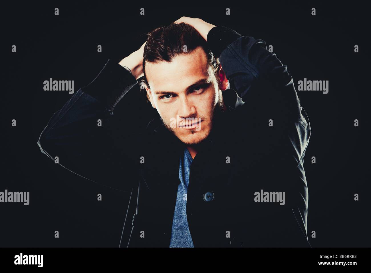 Nahaufnahme des jungen bärtigen Mannes auf dunklem Hintergrund modernes und dramatisches Foto. Das männliche Model trägt blaues T-Shirt und eine schwarze Jacke, Toront Stockfoto