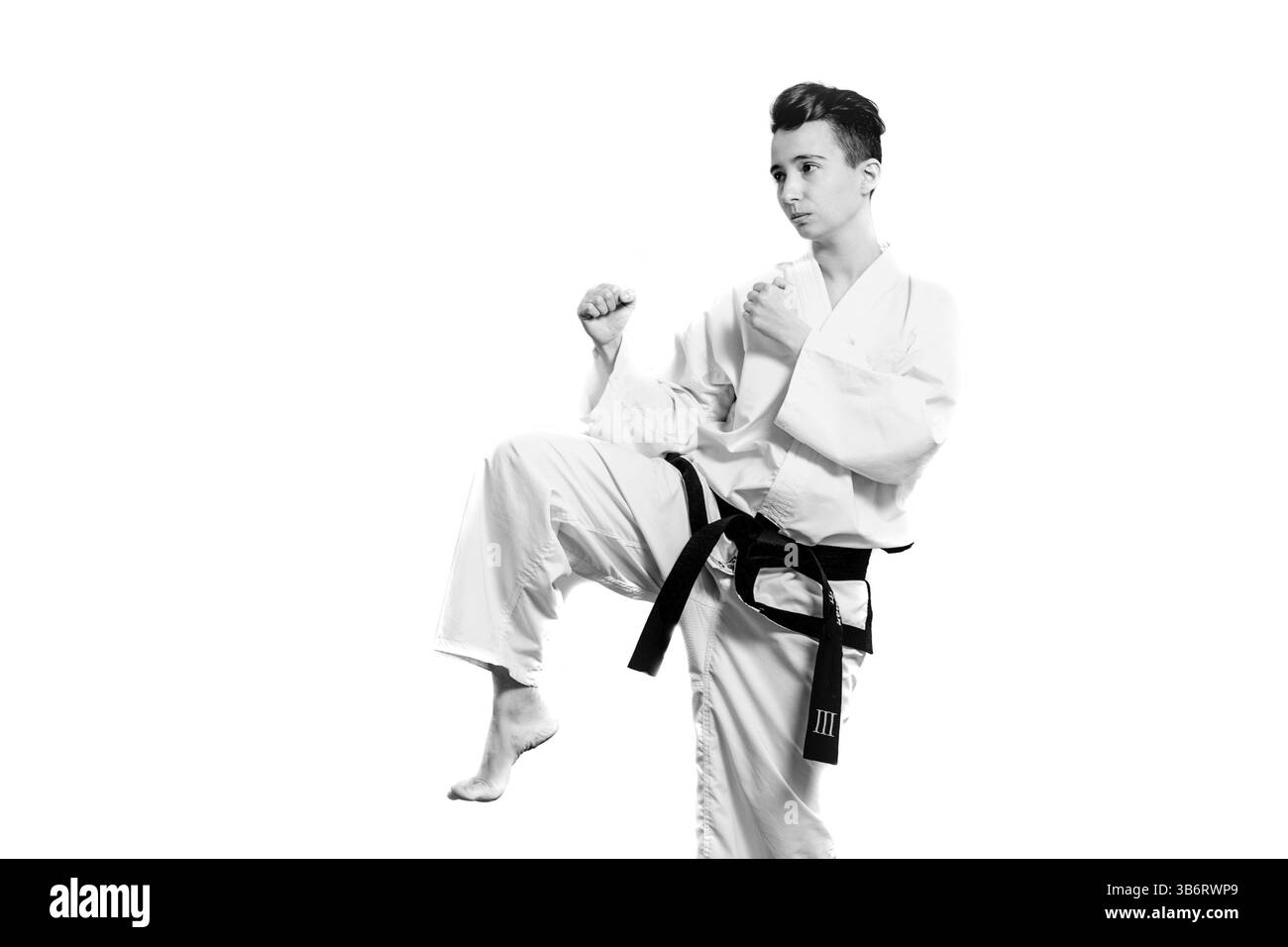 Mädchen im Karate-Anzug-Kimono im Studio auf grauem Hintergrund. Das weibliche Kind zeigt Judo oder Karate stans in weißer Uniform mit schwarzem Gürtel. Individual Martial Stockfoto