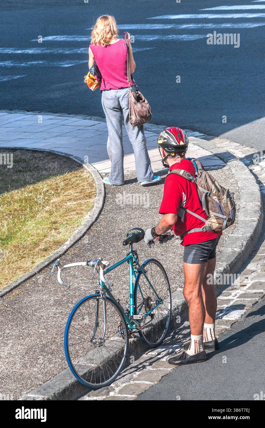 Älterer Mann mit Fahrrad, der jüngere Frau an der Straßenecke ansieht. Stockfoto