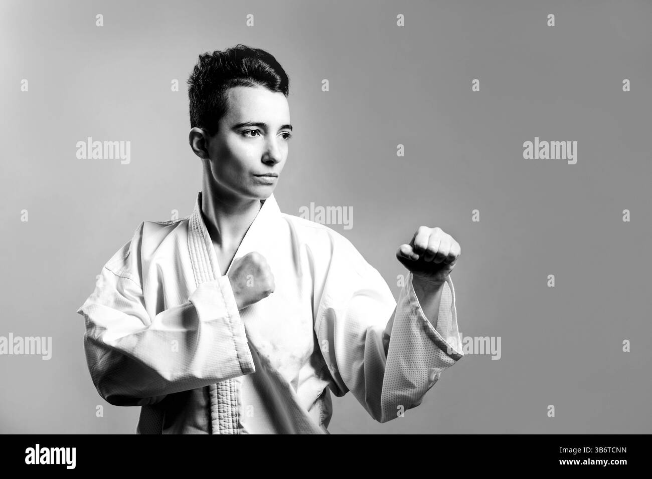 Mädchen im Karate-Anzug-Kimono im Studio auf grauem Hintergrund. Das weibliche Kind zeigt Judo oder Karate stans in weißer Uniform mit schwarzem Gürtel. Individual Martial Stockfoto
