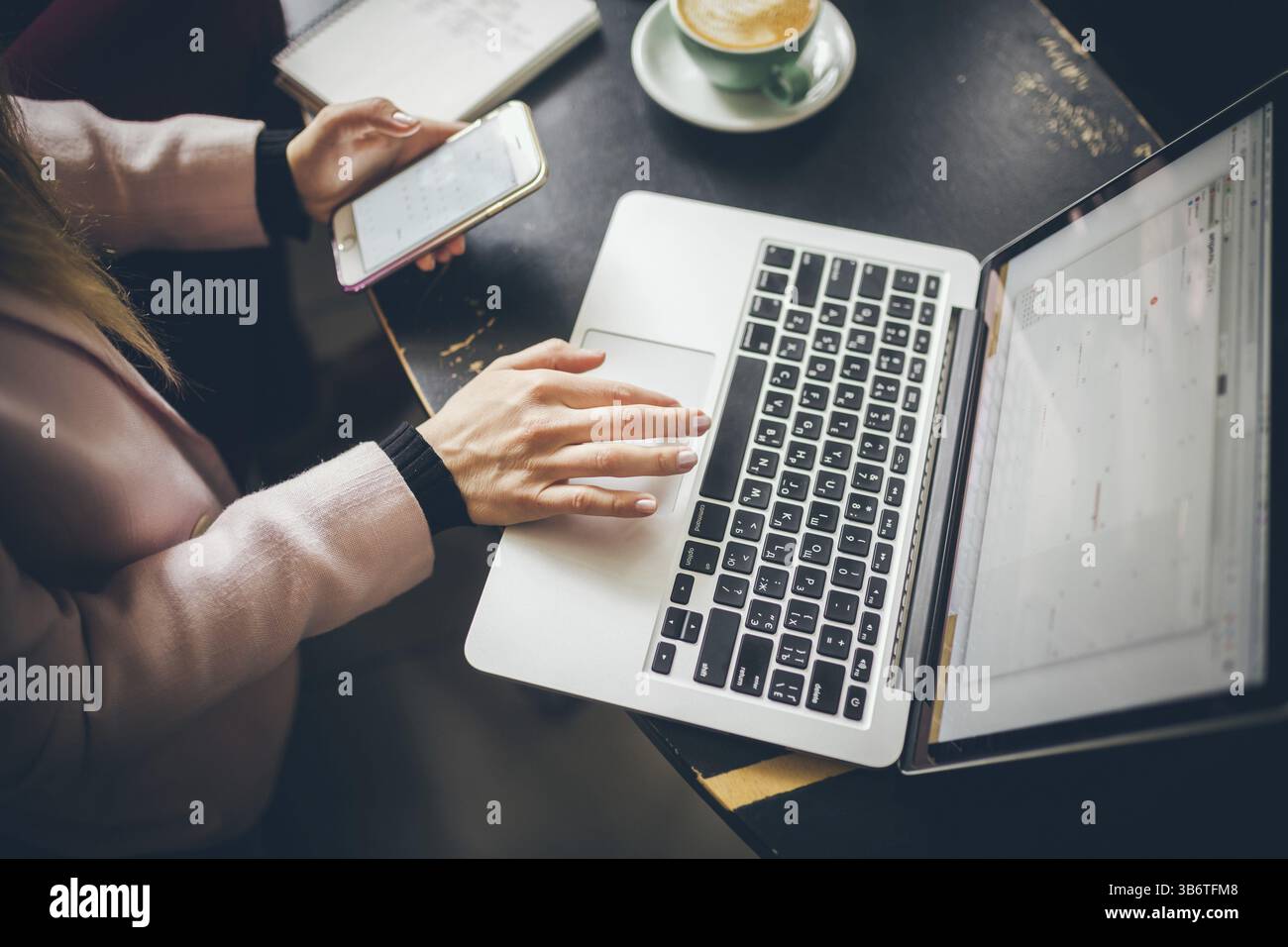 Close-up Ansicht von oben in die Hände des Kaukasischen Frau lässig gekleidet, Student, Blogger, Autor Mann, der an einem Notebook arbeitet mit einem Handy in der Hand, im Inneren der Stockfoto