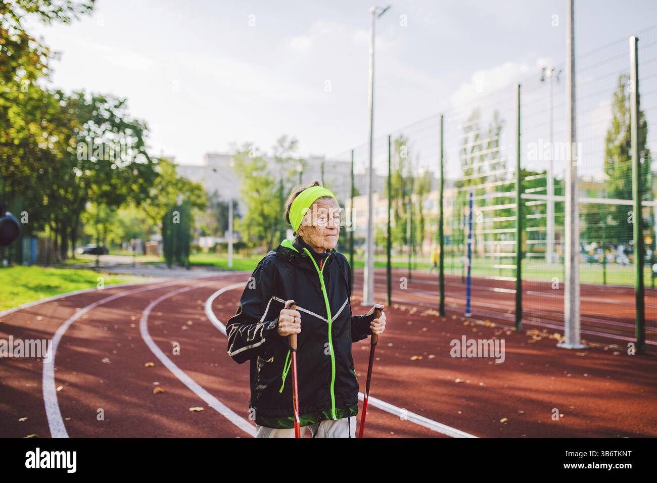 Alte Frau in Sportbekleidung, die im Stadion nordic Walking auf einem Gummiband praktiziert. Ältere Frauen gehen mit einem skandinavischen Spaziergang mit einem Trekkingstock Stockfoto