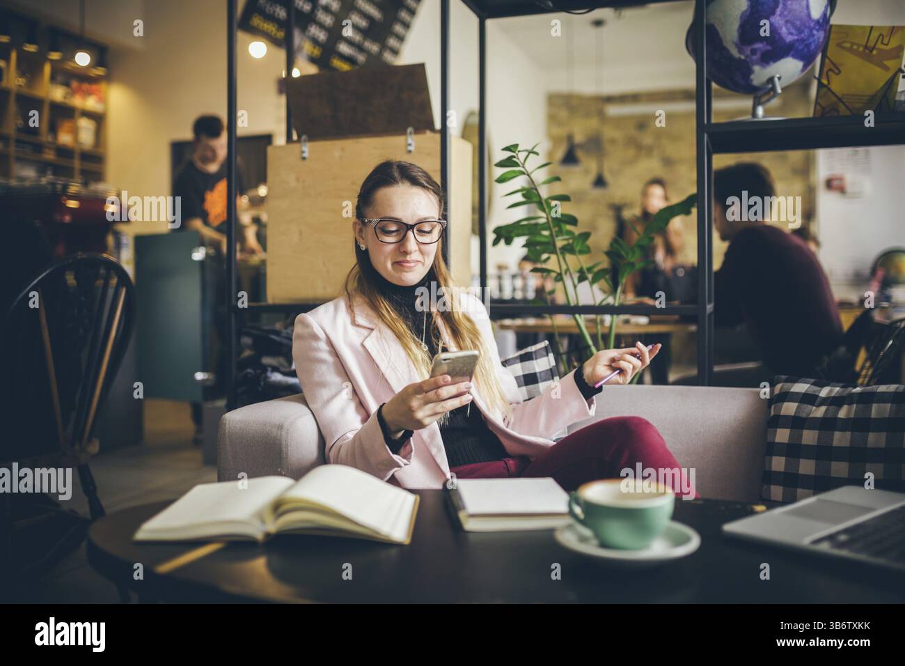Thema moderner Beruf Bloggerin. Kaukasische Frau mit Brille und Jacke sitzt im Café hinter Holztisch mit Notizbuch, Laptop A Stockfoto