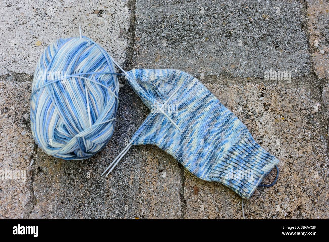 Hellblaues Sockengarn, das zum Stricken von Socken verwendet wird, mit Stricknadeln, die auf einer Steinoberfläche liegen Stockfoto