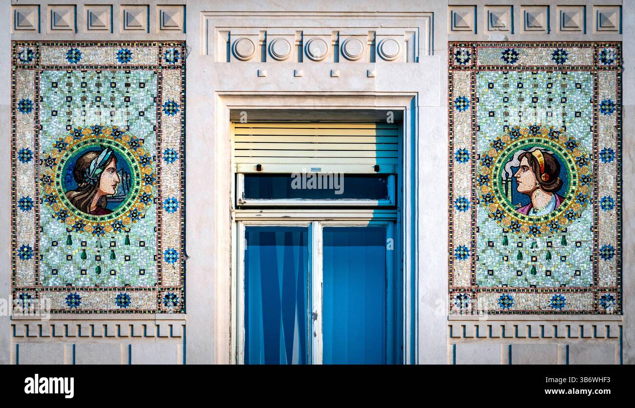 Eine dekorative Fassade mit komplexen Mosaikkunstwerken auf beiden Seiten eines Fensters. Die Mosaike zeigen zwei stilisierte weibliche Figuren, umgeben von Farben Stockfoto