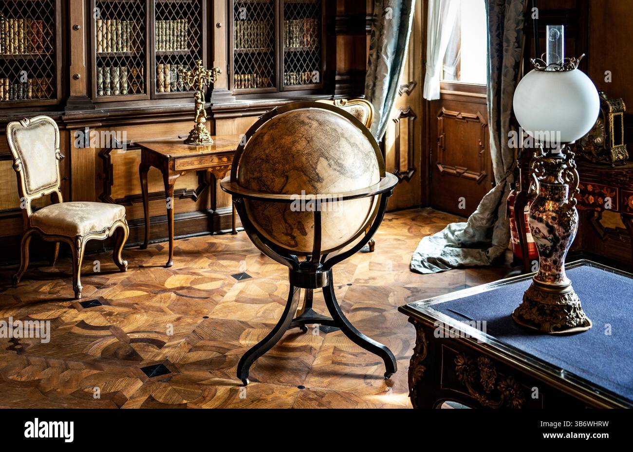Ein Vintage-Globus an einem Stand in einer eleganten Bibliothek, umgeben von antiken Möbeln und warmer Beleuchtung. Stockfoto