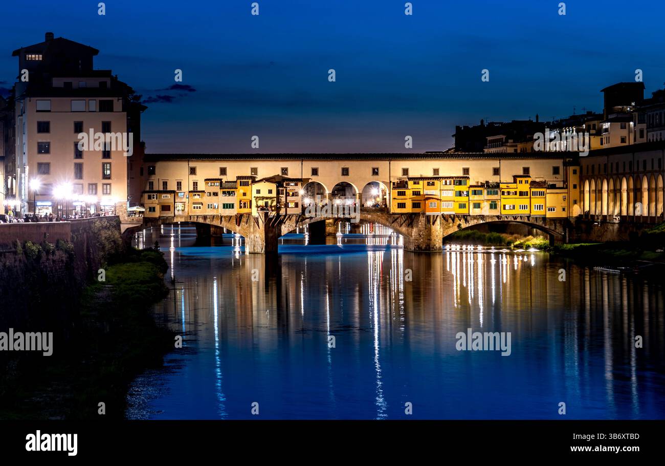 Ein atemberaubender Blick bei Nacht auf die Brücke Ponte Vecchio in Florenz, Italien, beleuchtet vor einem Abendhimmel. Die Reflexion der Brücke und der Gebäude i Stockfoto