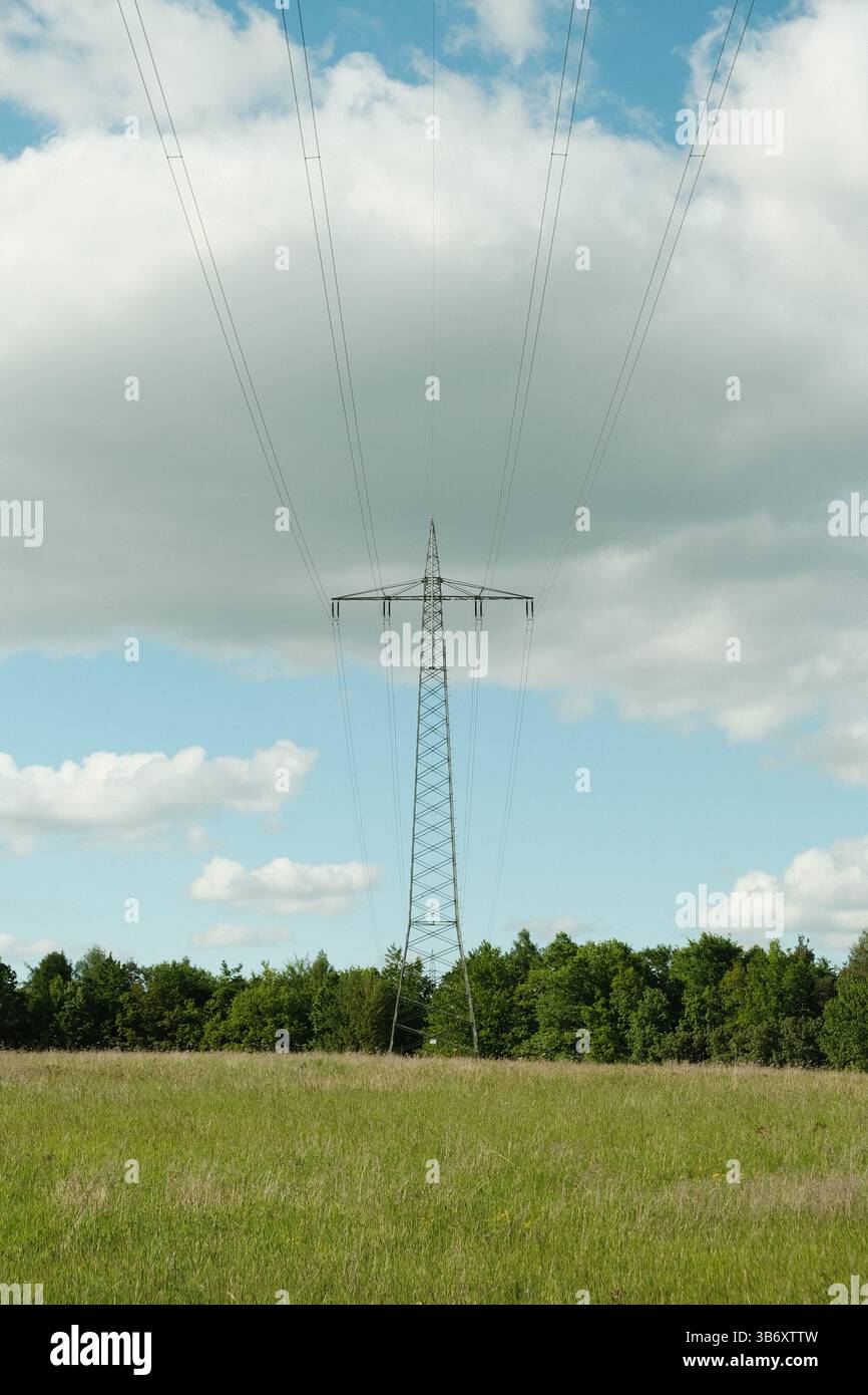 Freistehender Hochspannungspylon in Deutschland mit Stromleitungen, grünem Vordergrund und blauem Himmel. Stockfoto