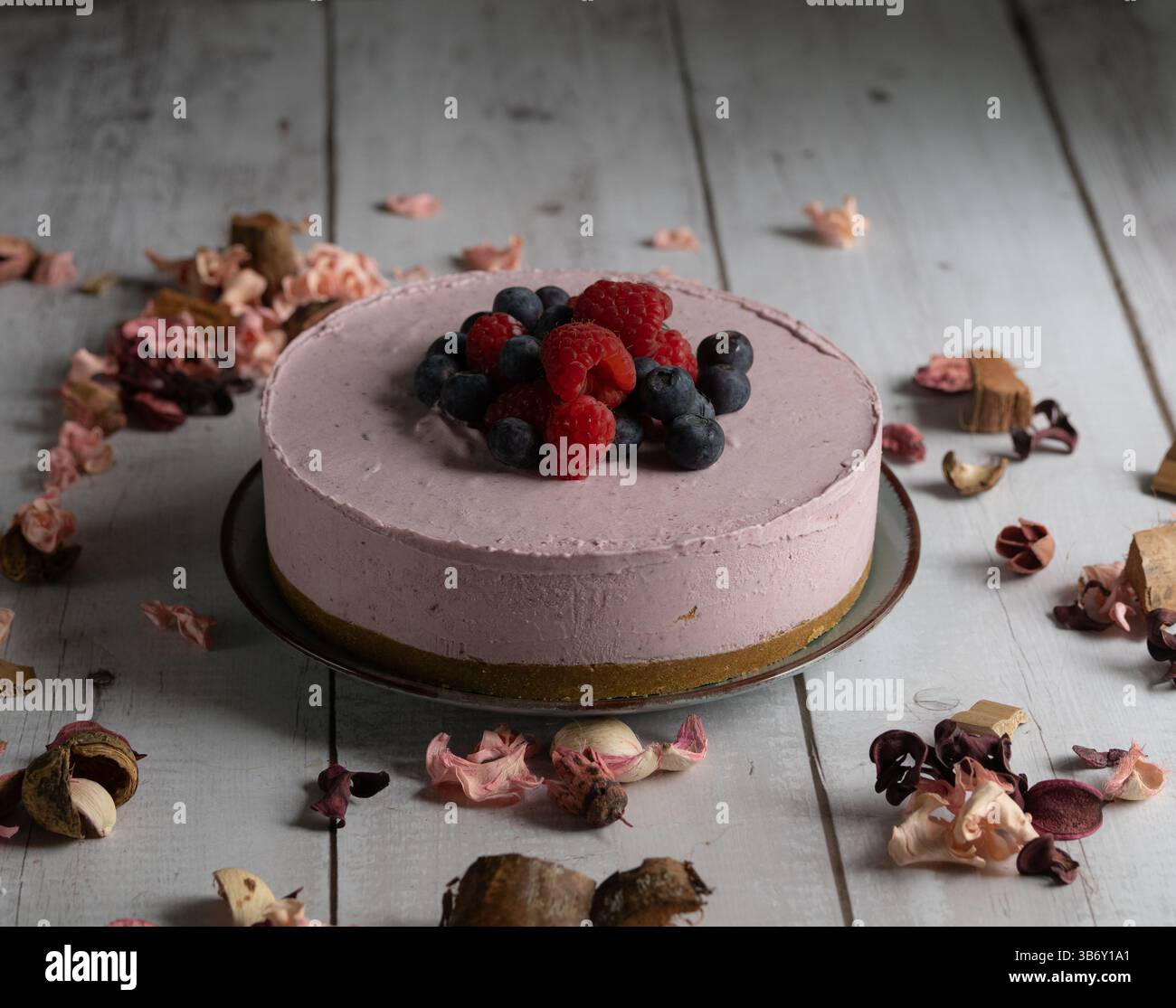 Horizontales Foto von einem gefrorenen roten Obstkuchen mit Blumendekorationen in einer rustikalen und romantischen Umgebung. Stockfoto