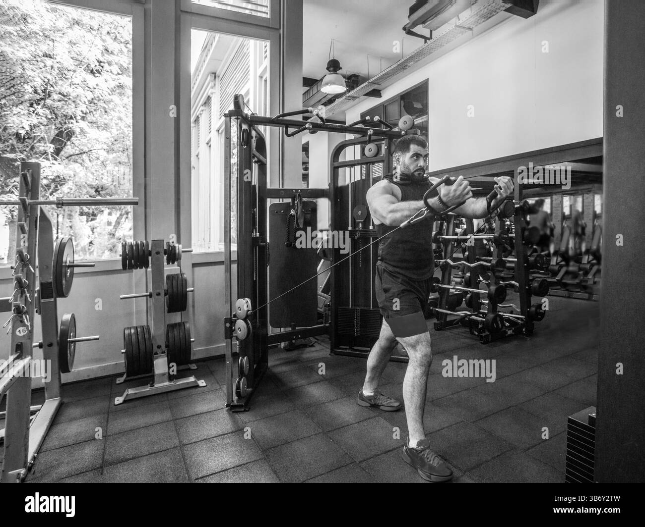 Ein junger starker Mann trainiert in einem Fitnessstudio auf einem Simulator. (Trizepstraining) Schwarz-weiß Stockfoto